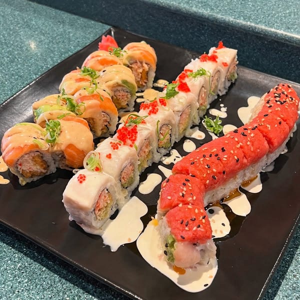 Three rows of colorful sushi rolls with various toppings and sauces on a black plate.