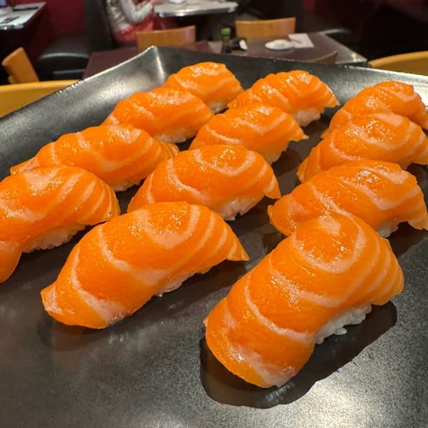 A black rectangular plate filled with rows of vibrant orange salmon nigiri sushi.