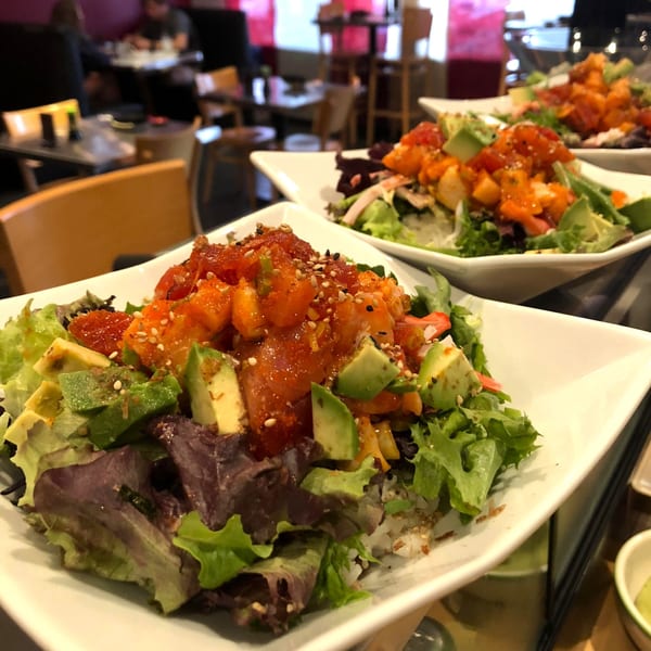 Three vibrant poke bowls with salmon, avocado, and mixed greens on white plates at Sushi Avenue.