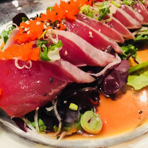 Sushi Avenue's tuna tataki with bright orange roe, green onions, and sesame seeds on a bed of greens.