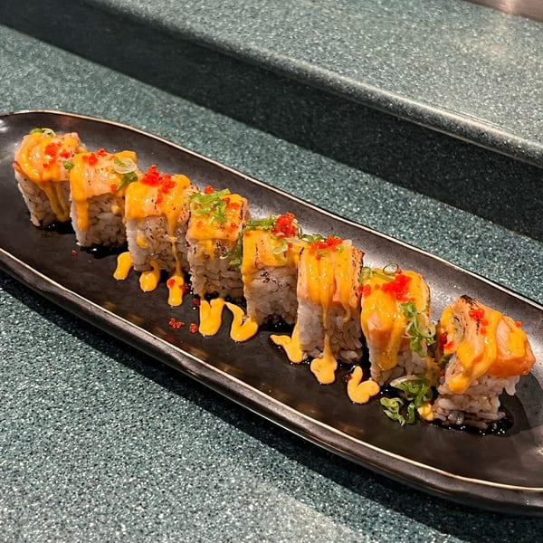 Sushi Avenue's baked salmon rolls with orange sauce, red roe, and green onions on a black plate.