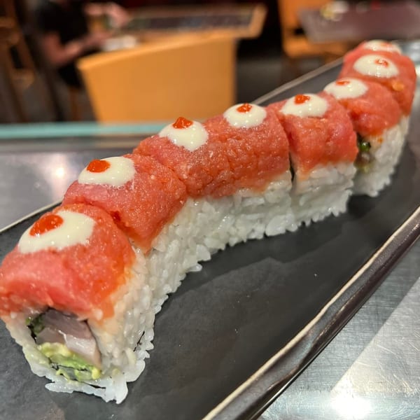 Sushi Avenue's tuna sushi roll, topped with white sauce and red dots, on a dark plate.
