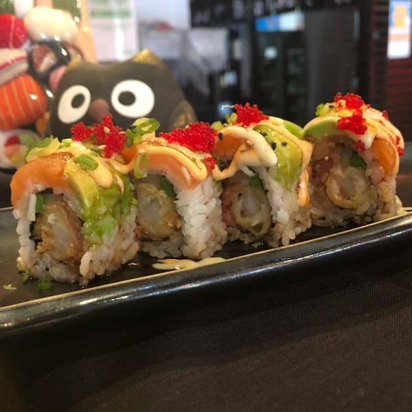 Four pieces of Sushi Avenue's special roll with salmon, avocado, and red roe on a black plate.
