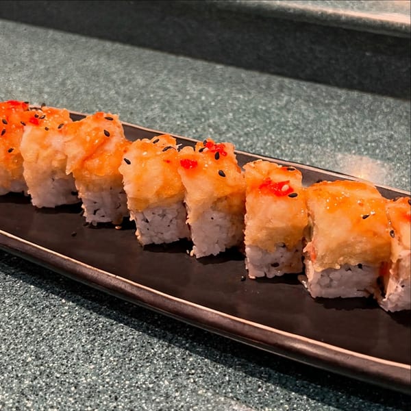 A row of Sushi Avenue's fried sushi rolls with orange sauce and black sesame seeds.